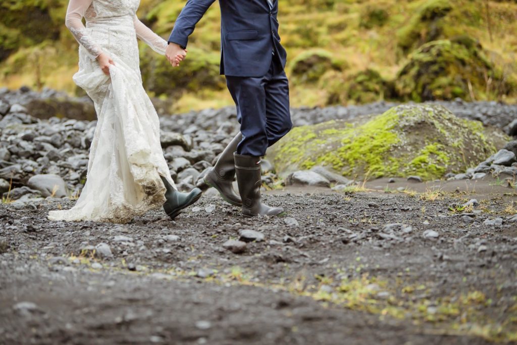 Eloping couple wearing white dress with rainbows and (groom) suite and rainboots in the mud