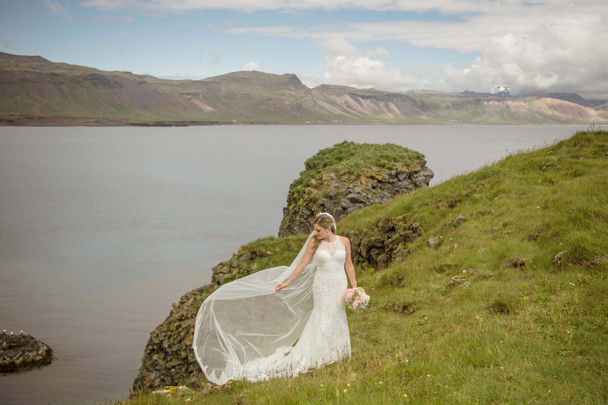 Bride in white mermaid-style dress against green, hilly landscape